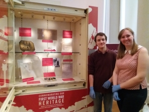 2 young people are wearing gloves and standing next to a museum case.