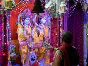 A man is looking and pointing at a case with hindu statues inside during Diwali.