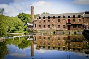a photograph of a water mill with the river in the foreground on a sunny day.