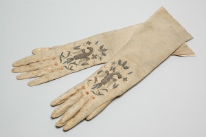 A pair of well worn gloves, with embroidery on the hand.