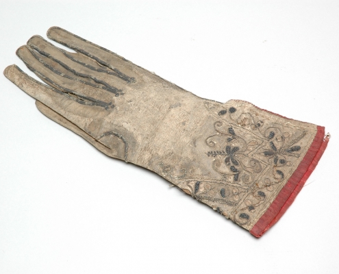 A glove that looks very worn, but has beautiful embroidery on the wrist.