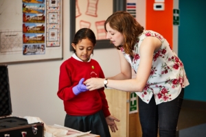 A woman is showing a young girl a museum object in a primary school classroom.