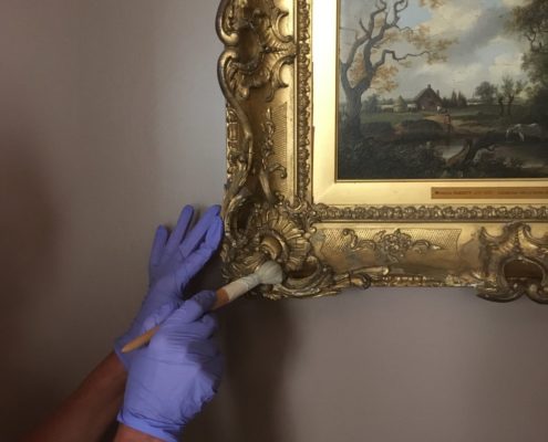 A hand wearing purple gloves is dusting a painting