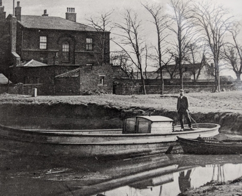 A black and white photo of a man in a boat on a pond outside Thwaite Watermill
