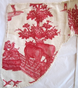 A piece of cotton with a pink printed countryside scene, featuring 2 cows 2 people in old fashioned dress and a tree