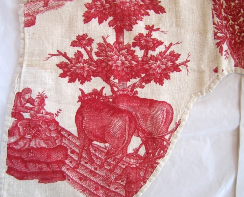 A piece of cotton with a pink printed countryside scene, featuring 2 cows 2 people in old fashioned dress and a tree