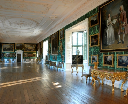 a very long ornate gallery space in an old building. The wallpaper is green and there are lots of portraits on the wall.
