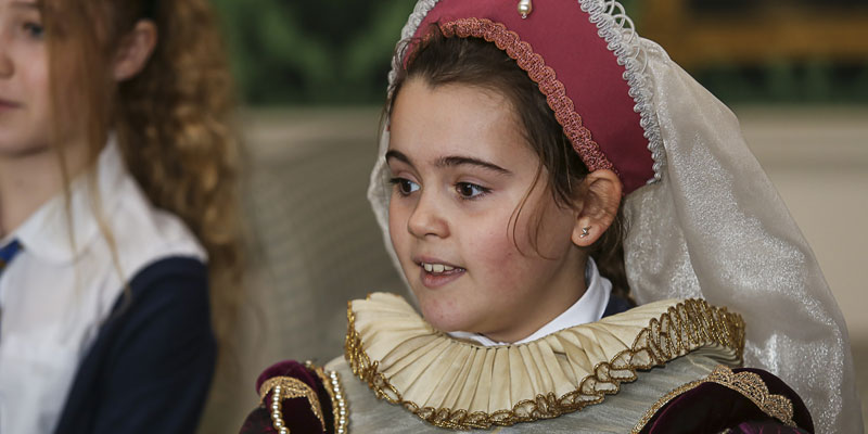 A young girl is dressed in traditional Tudor costume including head wear and a ruff