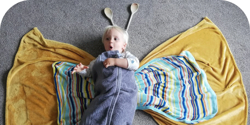 A toddler wrapped in towels and blankets in the shape of a large butterfly