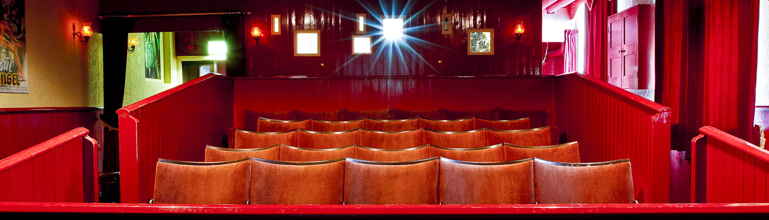 The red interior of an old 1220s cinema with the light from a projector shining in the background