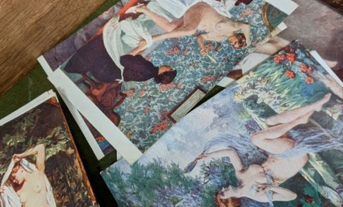 A collection of classical nude postcards laid out on a wooden table