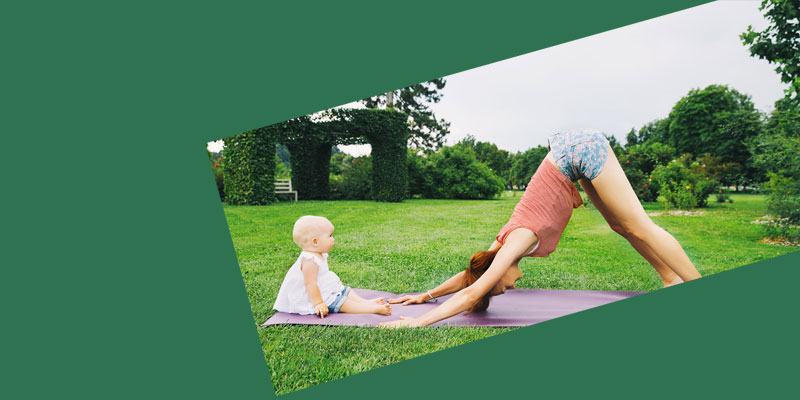 A baby and parent doing yoga outdoors.