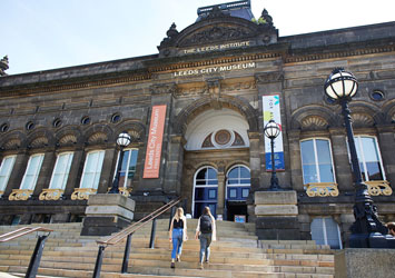 Two people walking up the steps to the entrance of Leeds City Museum.