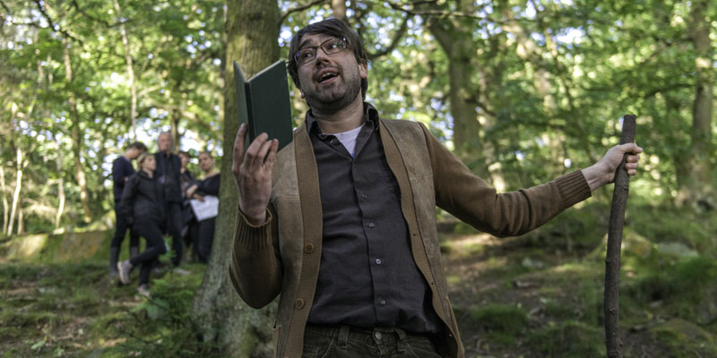 A man reading a book out loud in the woods