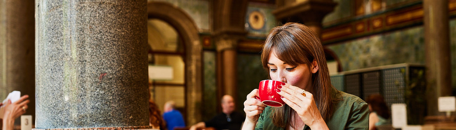 A woman drinks from a red cup in the Tiled Hall Cafe