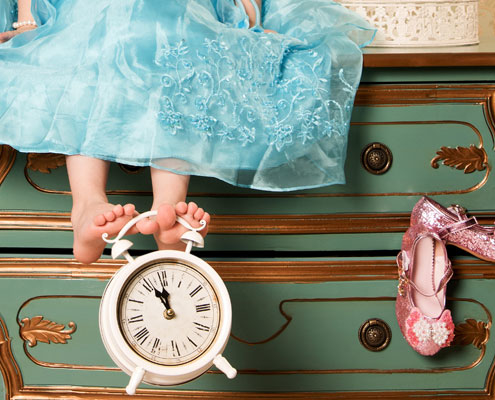 A young girl in a dress holding a clock which shows 11.55 depicting the Cinderella story.