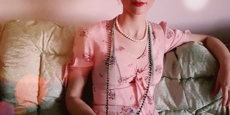 A woman wearing a vintage dress and beads sat on a sofa