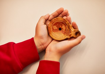 Hands of a child in school uniform holding a piece of pottery