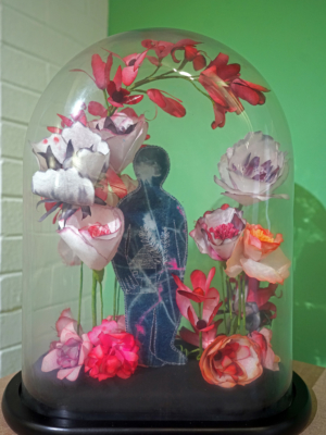 An artwork of a lone man in a glass case surrounded by paper flowers