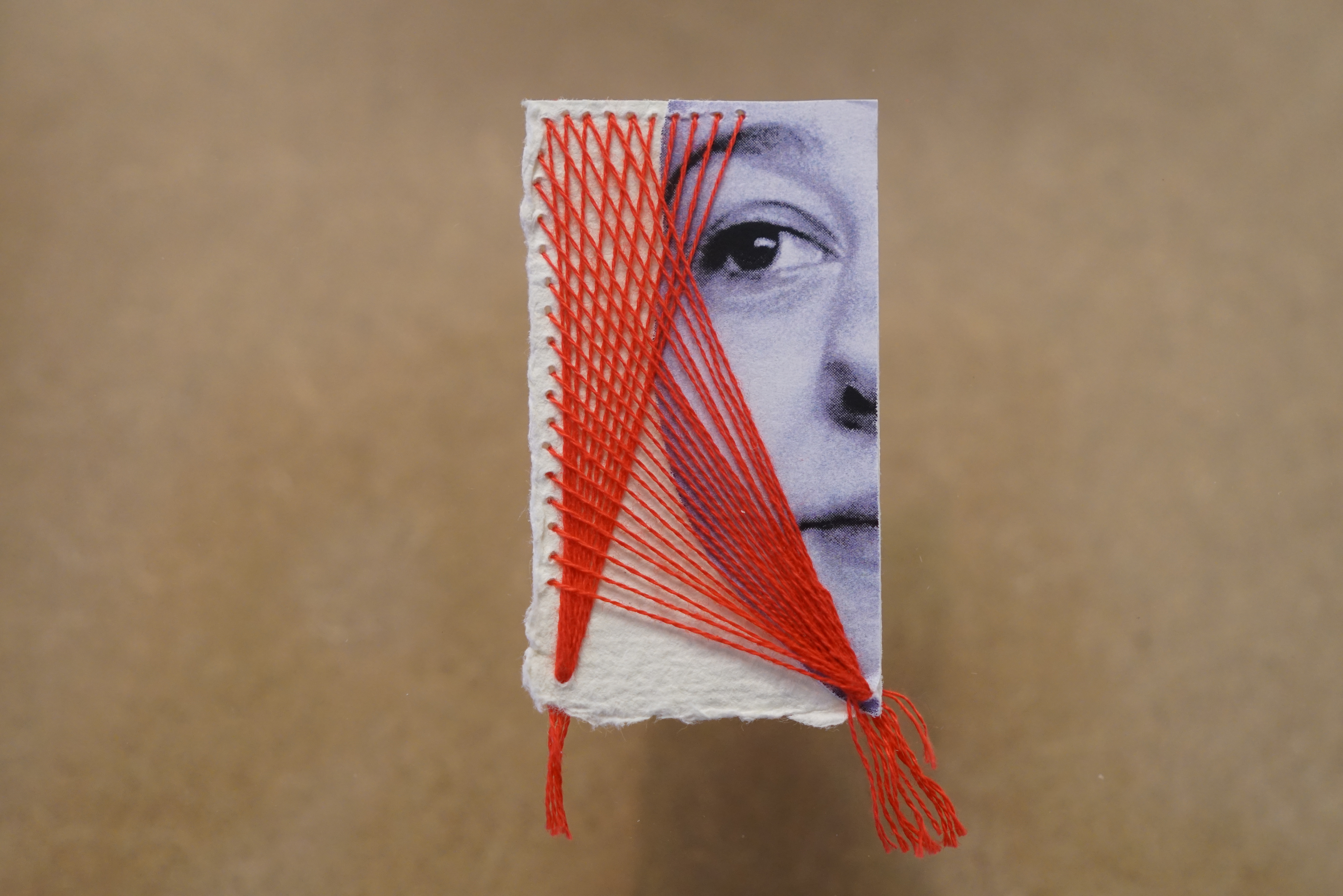 An intricate detail of a sketched face with red stitching set against a light wood background