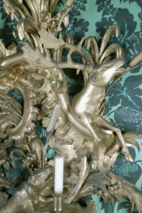 Close up of a candlestick holder on a wall. It's gold and shows a deer being chased by dogs.