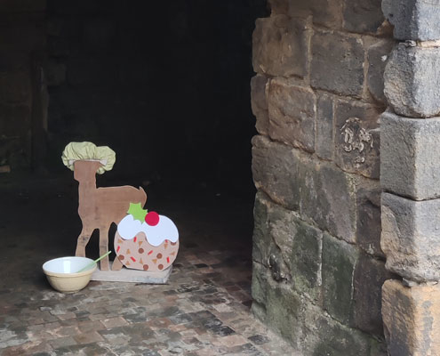 A wooden reindeer dressed in a cooks hat with a mixing bowl and a large christmas pudding at Kirkstall Abbey