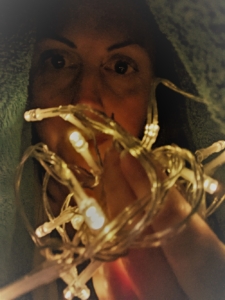 A woman under a towel is holding fairy lights