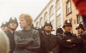 A photograph of a man with crossed arms in front of lots of policemen