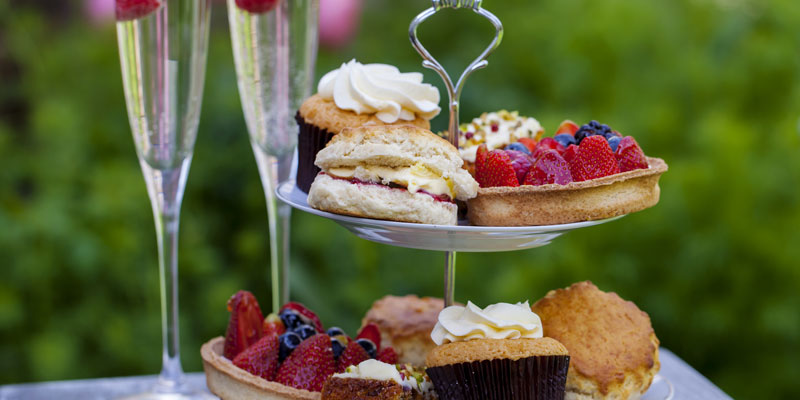 A selection of cakes and scones as part of an afternoon tea with fizzy wine in the background