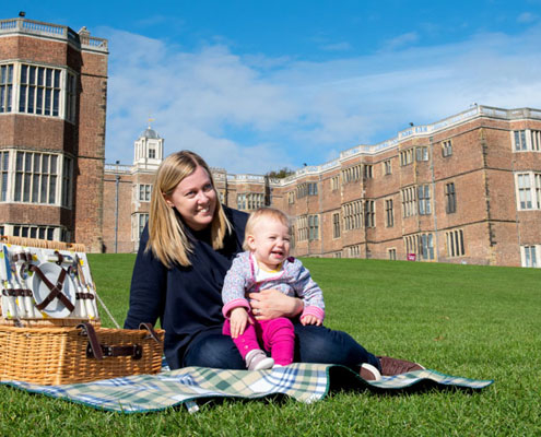 A mother and her baby enjoy a traditional picnic on the lawn against the backdrop of Temple Newsam House and a bright blue sky