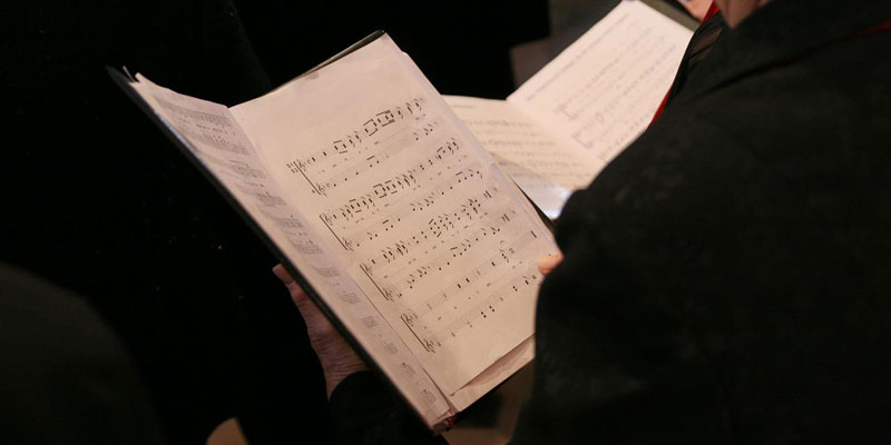 A choir book is being held up by a singer dressed in black