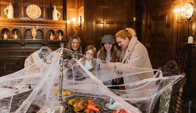 A family of four look at a table which is decorated with spiderwebs for Halloween