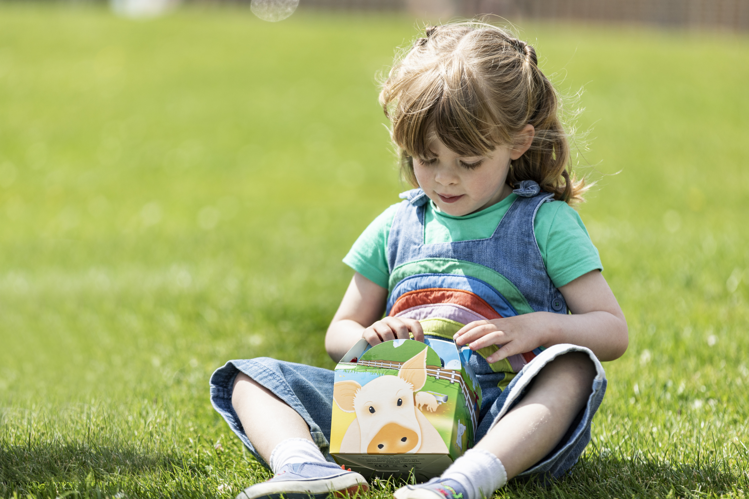 A little girl is sat on the grass holding a children's picnic box