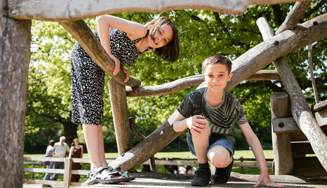 a young boy and girl climbing on a wooden playground