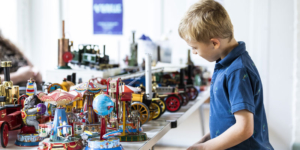 A young boy dressed in a blue t-shirt looks at old metal toys displayed on a table