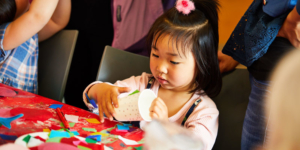 Young girl using paper cups surrounded by craft materials