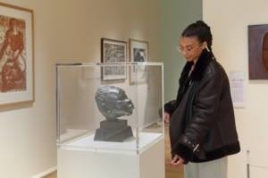 A woman is looking at a sculpture in a glass case of the head of a boy in a gallery