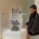 A woman is looking at a sculpture in a glass case of the head of a boy in a gallery