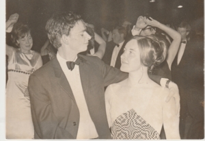 A black and white photograph of a man and a woman looking at each other and wearing eveningwear