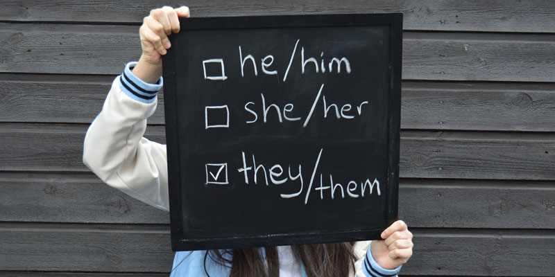 Person holding up a chalkboard with personal pronouns and tick boxes