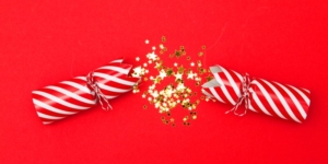 A red and white striped Christmas cracker broken in half with sparkly stars inside, on a red background