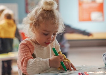 A young child drawing with a green pen