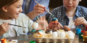 Two children using paintbrushes to decorate eggs