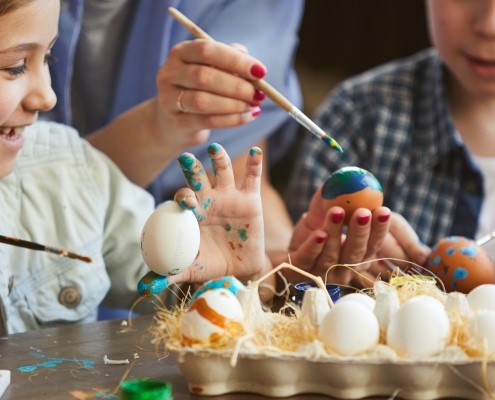 Two children using paintbrushes to decorate eggs
