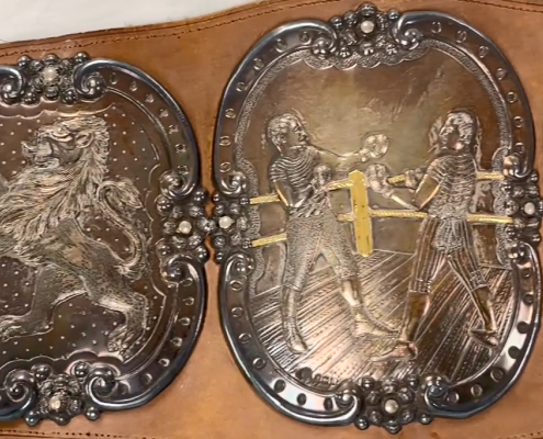 A wide brown leather belt with engraved silver plaques, depicting lions and boxers in a boxing ring