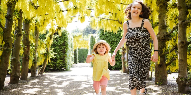 Two girls smiling and running towards the camera with yellow flowers behind