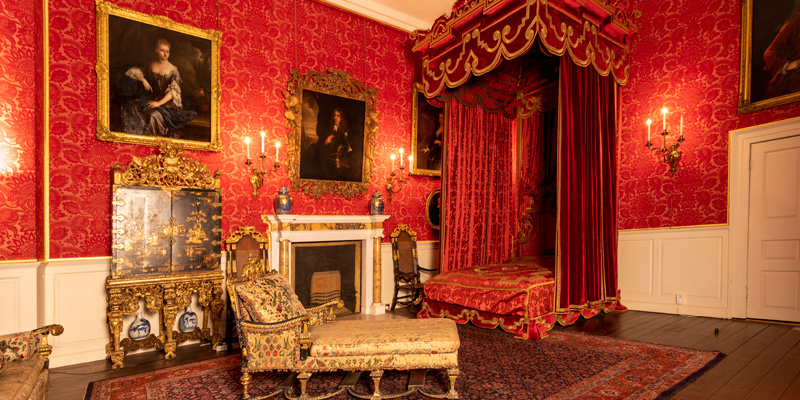 Crimson bedroom at Temple Newsam with ornate furniture, wallpaper and decorative art.
