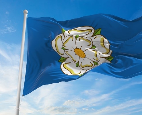 A yorkshire flag (white rose on a blue background) flying in the wind with blue sky behind