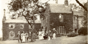 Old photograph is sepia of the exterior of Abbey House Museum with people in the foreground and ivy covering the museum walls