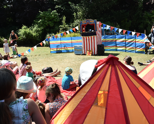 children watching a punch and judy show with red and yellow striped tent in foreground